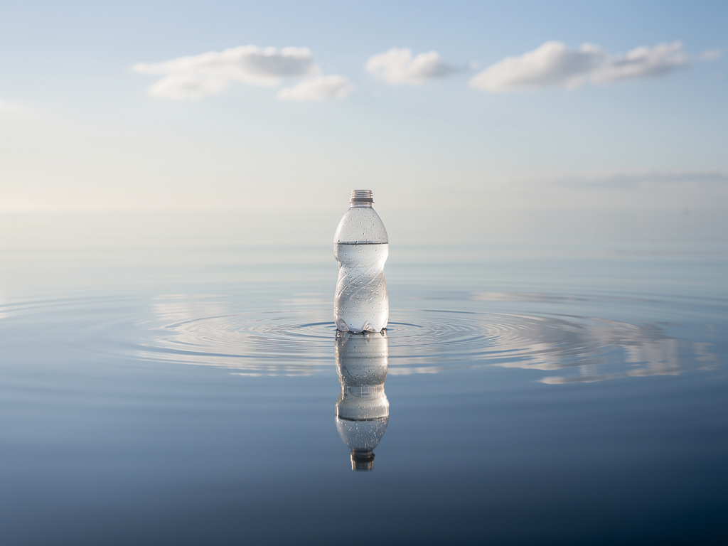 Durgun bir deniz yüzeyinde bir plastik su şişesi hafif hafif sallanmaktadır.