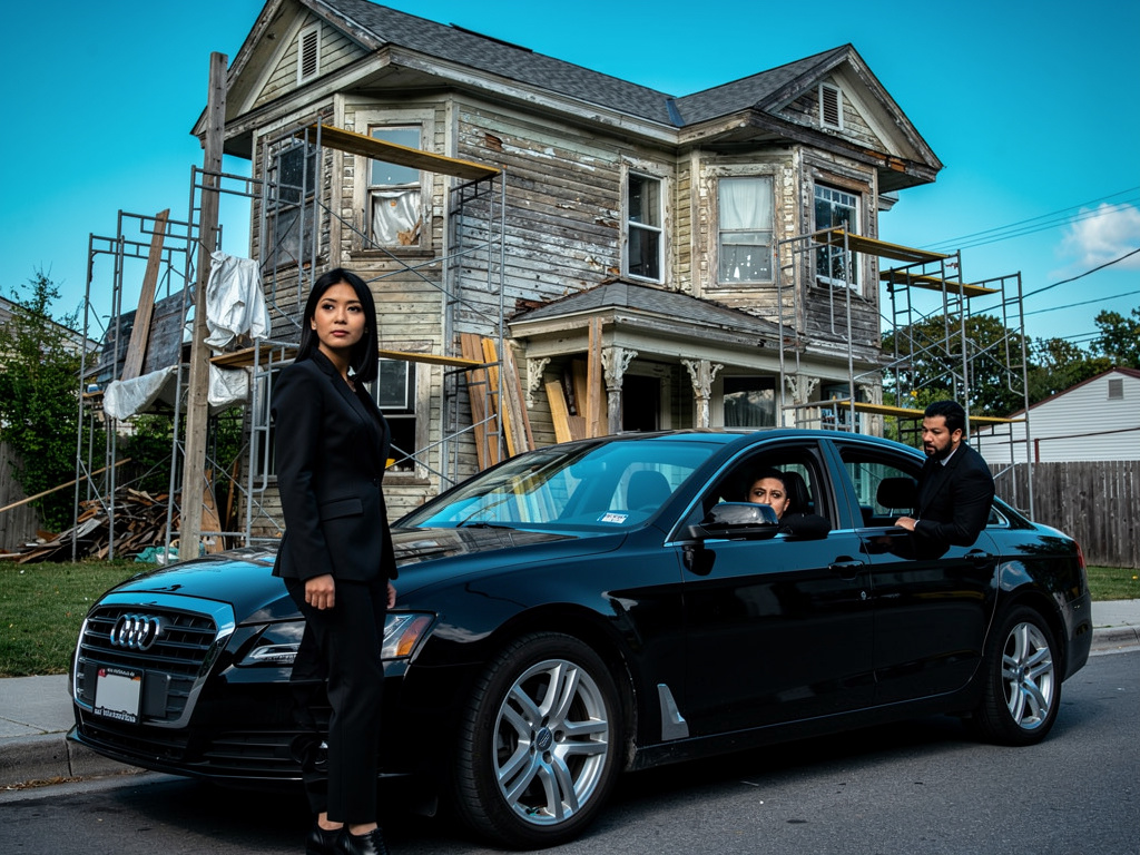 The sedan pulls up to an old, slightly dilapidated Victorian house, clearly undergoing renovation. Scaffolding is visible, bu